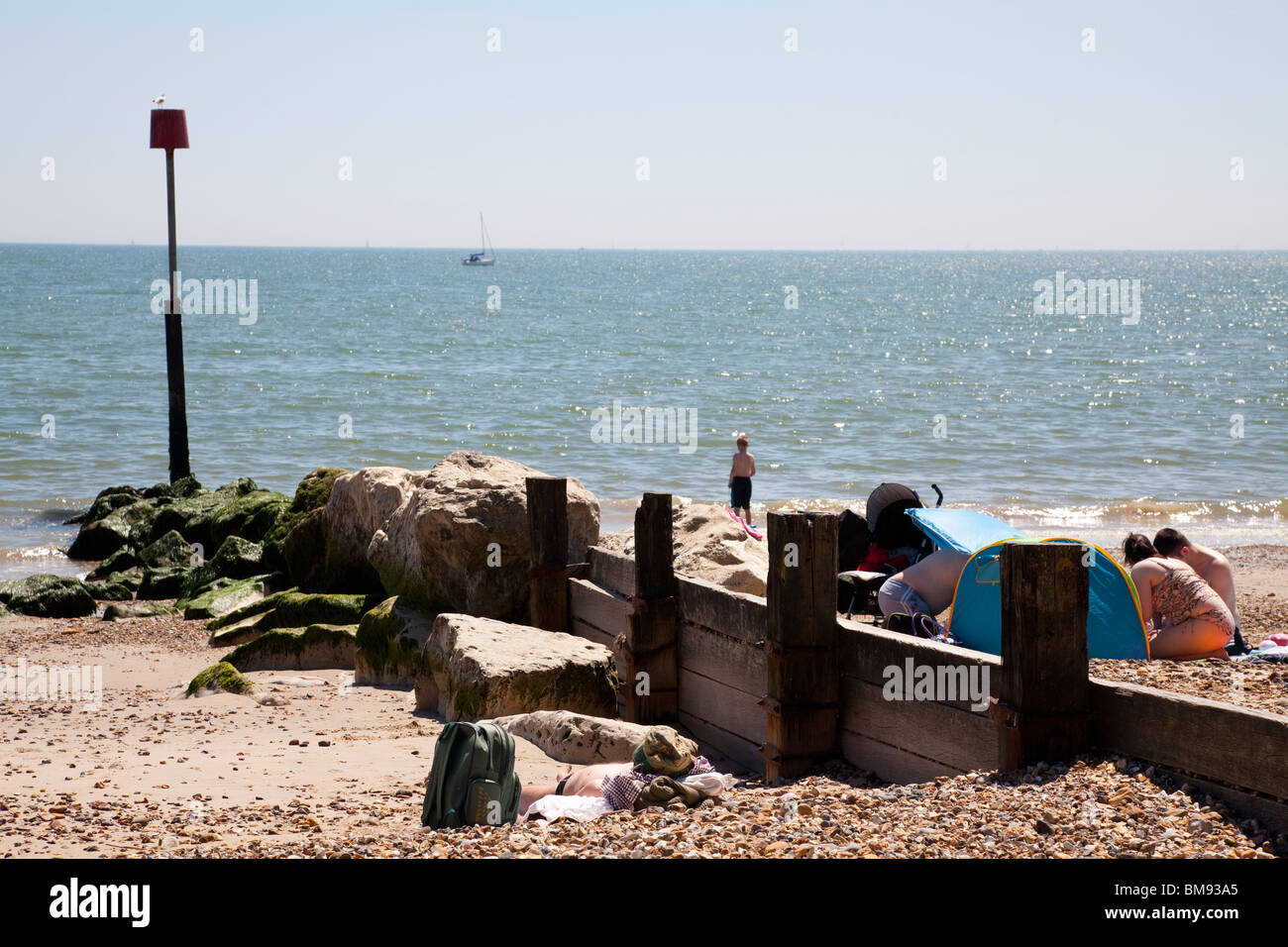 wooden and stone groyne with marker pole and sun seekers on beach at Mudeford Stock Photo