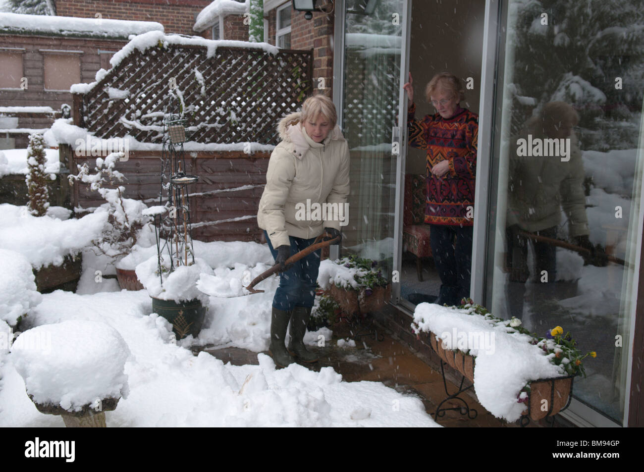 neighbour relative helping elderly person by clearing snow from path Stock Photo