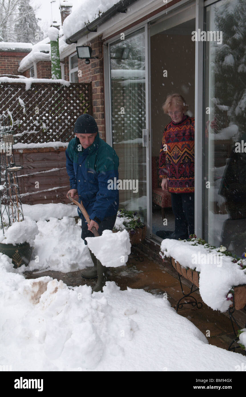 neighbour relative helping elderly person by clearing snow from path Stock Photo