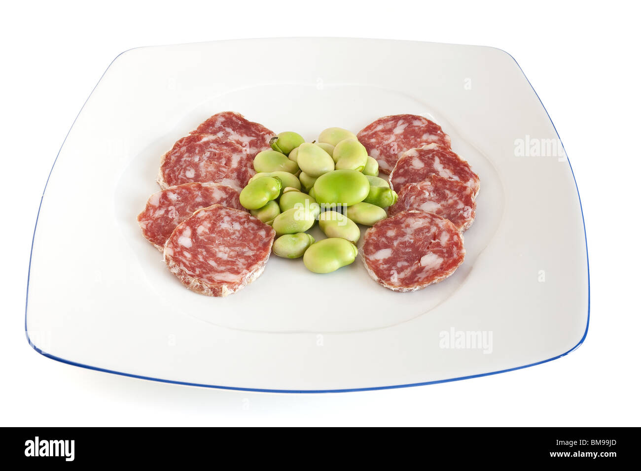 broad beans and salami sliced on a white plate isolated with clipping path Stock Photo