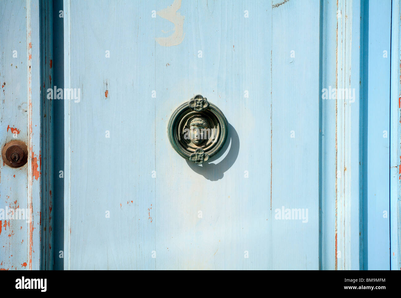 A blue door, flaking paint, door knocker with a centralised head of a young boy with a rusty lock, Gozo, Malta Stock Photo