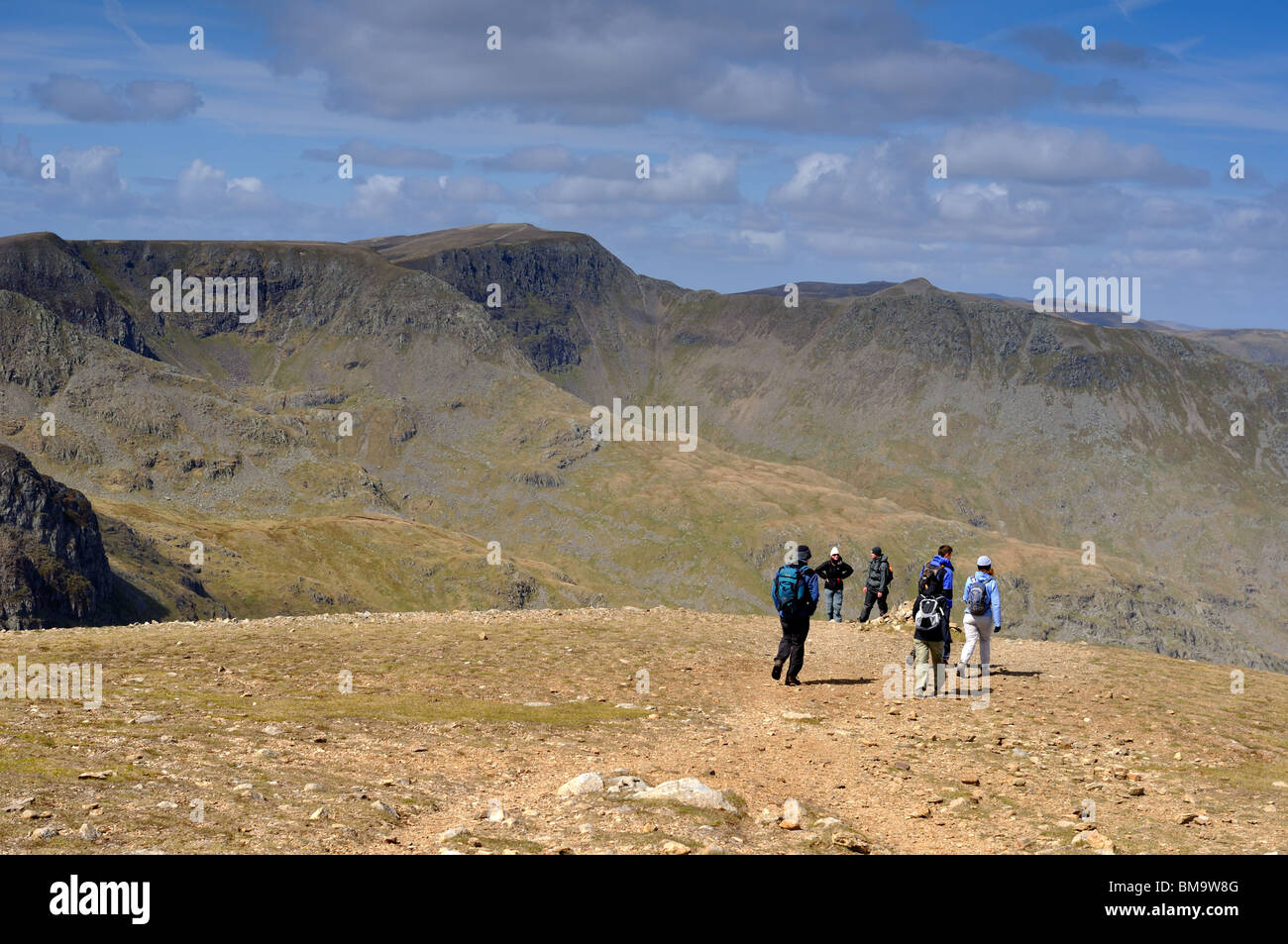 Walkers on the North West edge of Fairfield summit with the Hellvelyn range in the distance Stock Photo