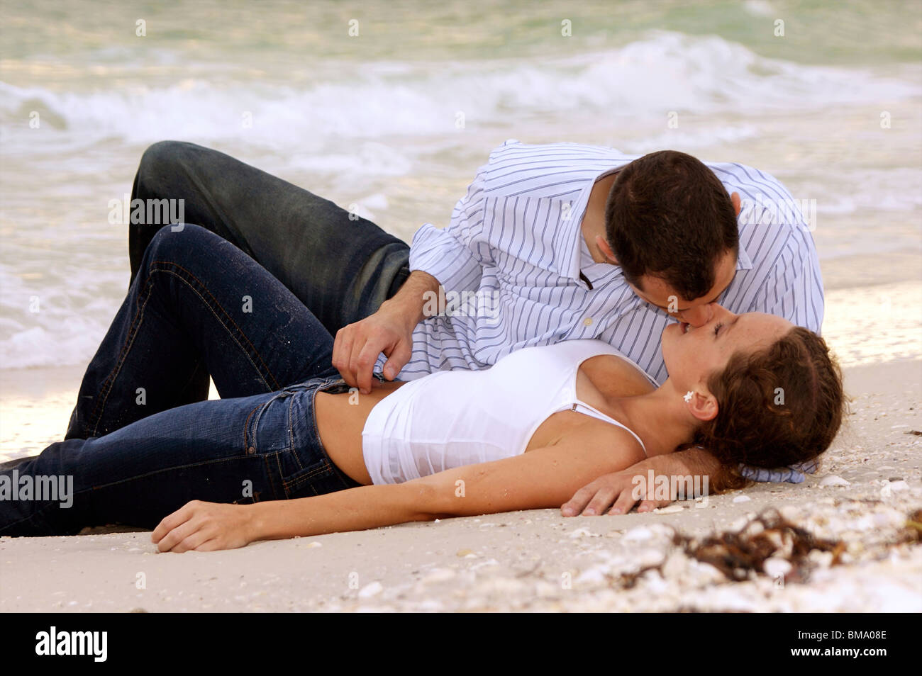 Beautiful sexy image of young couple in wet clothes laying on the beach  kissing Stock Photo - Alamy