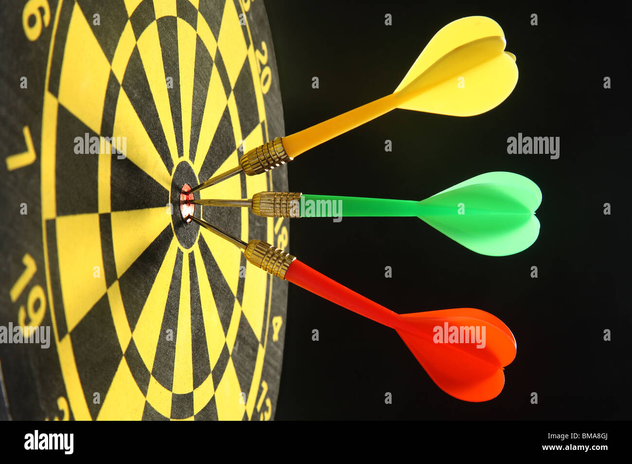 Three colourful darts in the bullseye Stock Photo Alamy