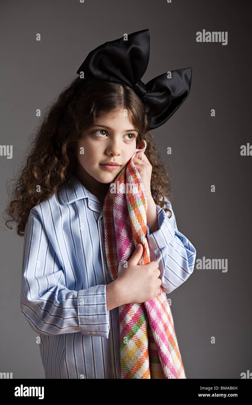 Young girl dressed in pyjamas with black hair bow, holding comfort blanket Stock Photo
