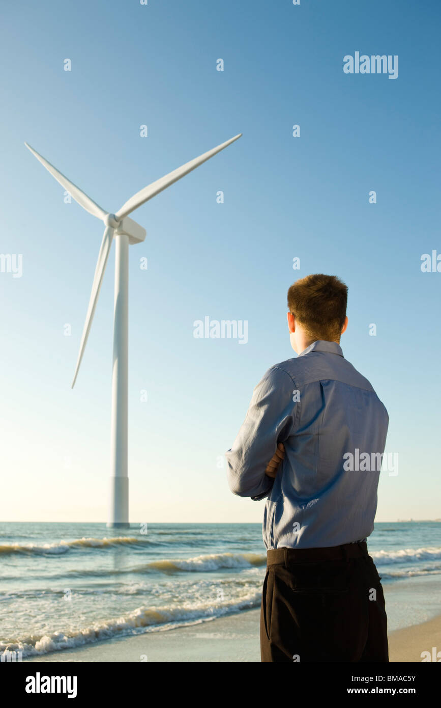 Businessman on beach looking at offshore wind turbine Stock Photo