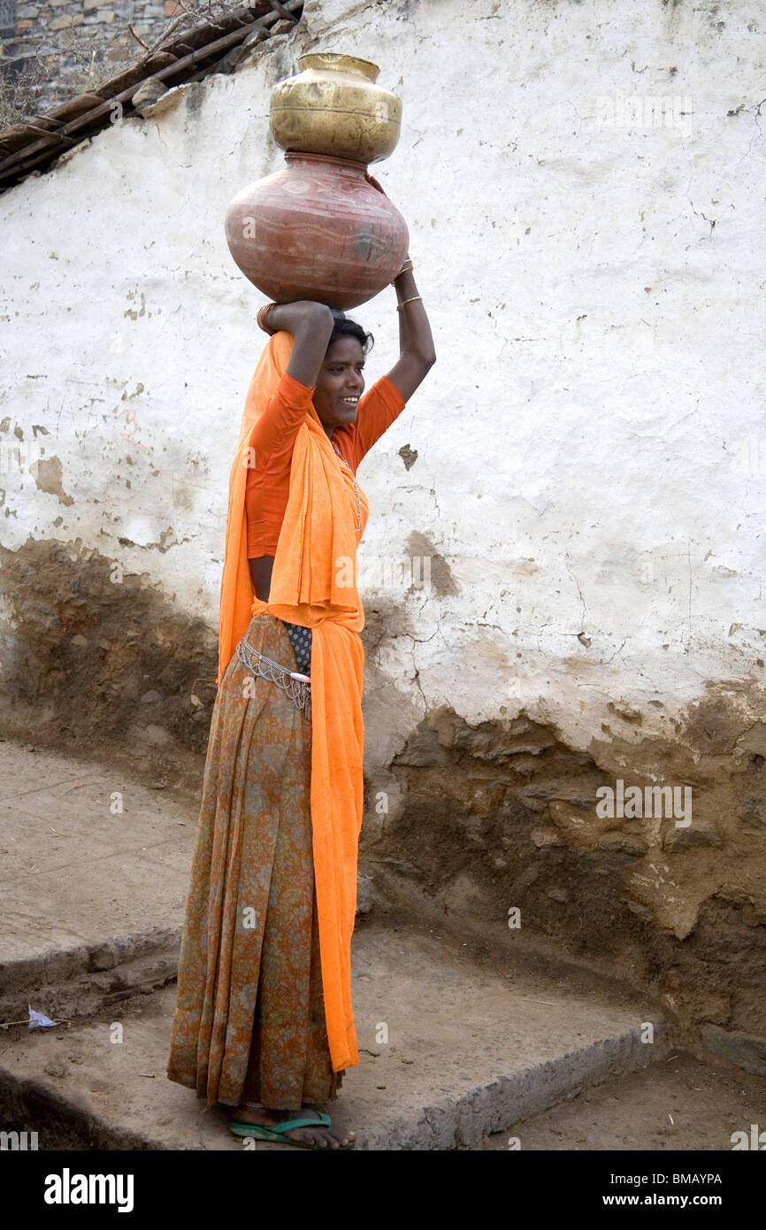 Rural woman carrying water in clay pot on her head standing in village
