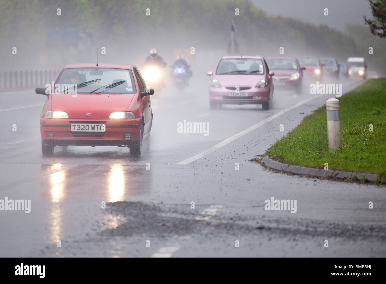 Dual carriageway road morning rush hour traffic on A75 bad weather rain mist spray motorcycles overtaking a line of cars UK Stock Photo