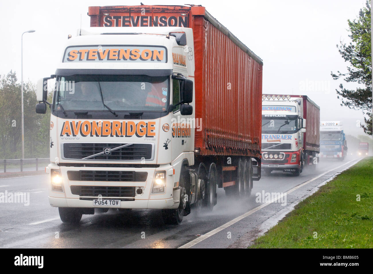 Rush hour traffic busy dual carriageway road A75 UK bad weather rain mist spray dark a line of lorries with lights on Stock Photo