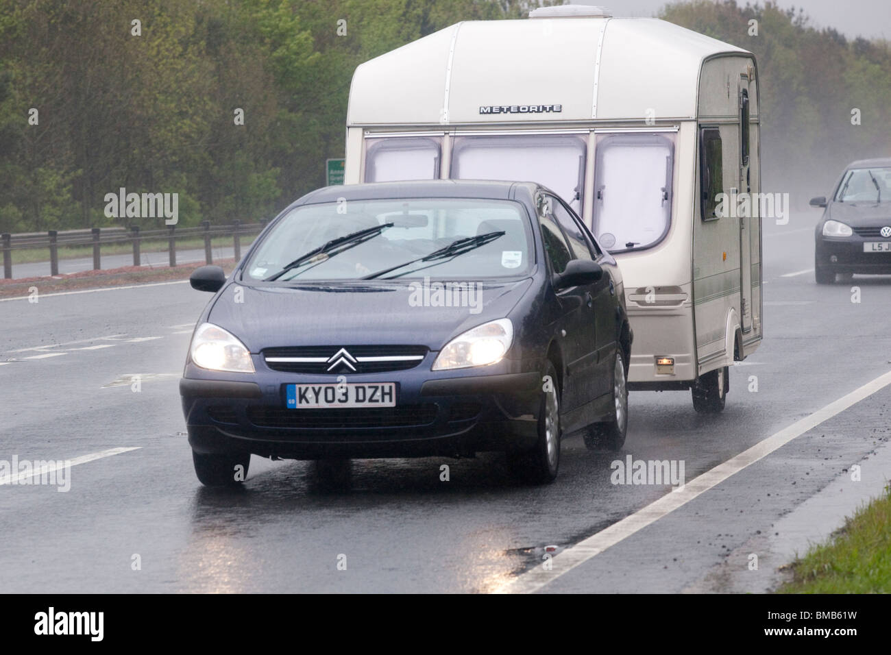 Dual carriageway road UK bad weather rain mist spray dark British summer time holidays car towing caravan in miserable weather Stock Photo