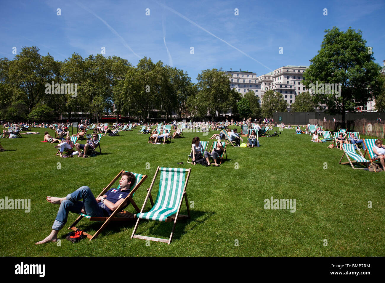 People lying on the grass and sitting on deck chairs in the sun at St