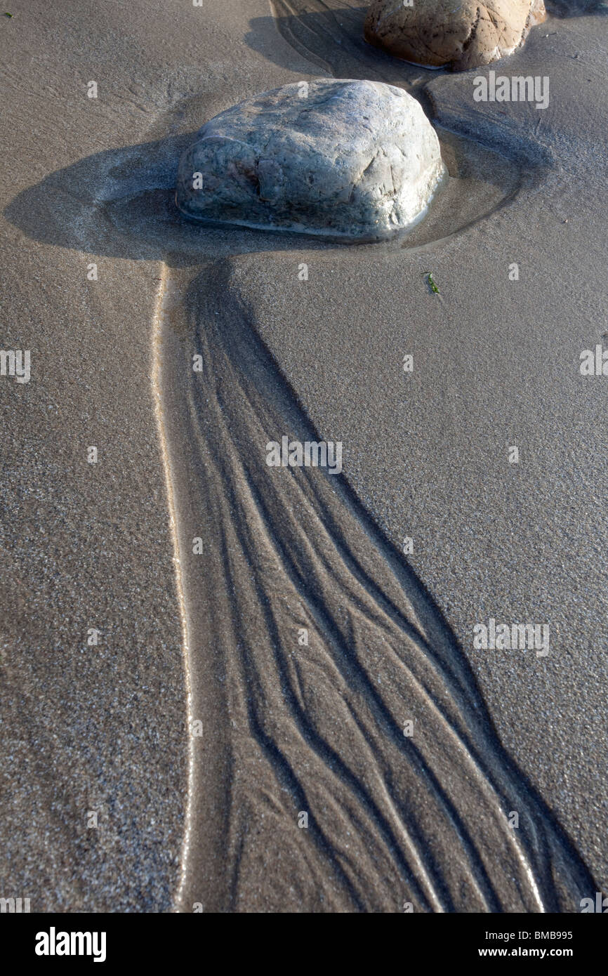 single pebble with patterns in sand made by retreating tide. Stock Photo