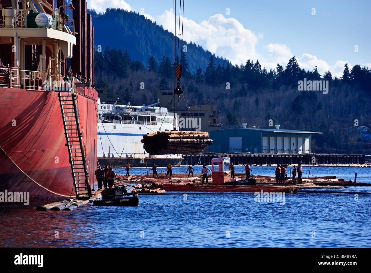 Lumber workers loading a ship with logs from a log boom alongside Stock Photo