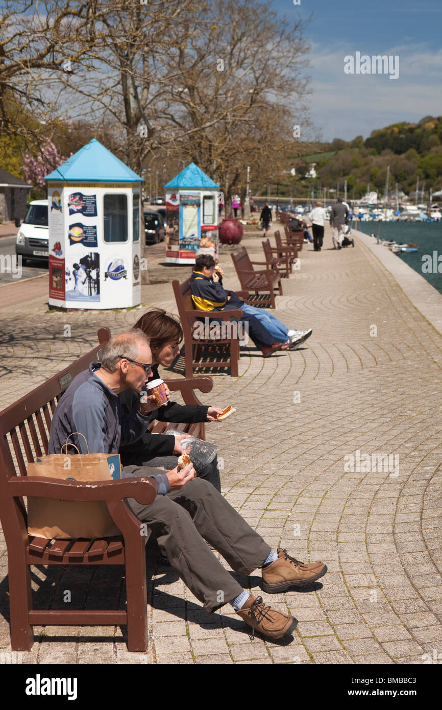 UK, England, Devon, Dartmouth, South Embankment, visitors sat in sunshine on banks of River Dart Stock Photo