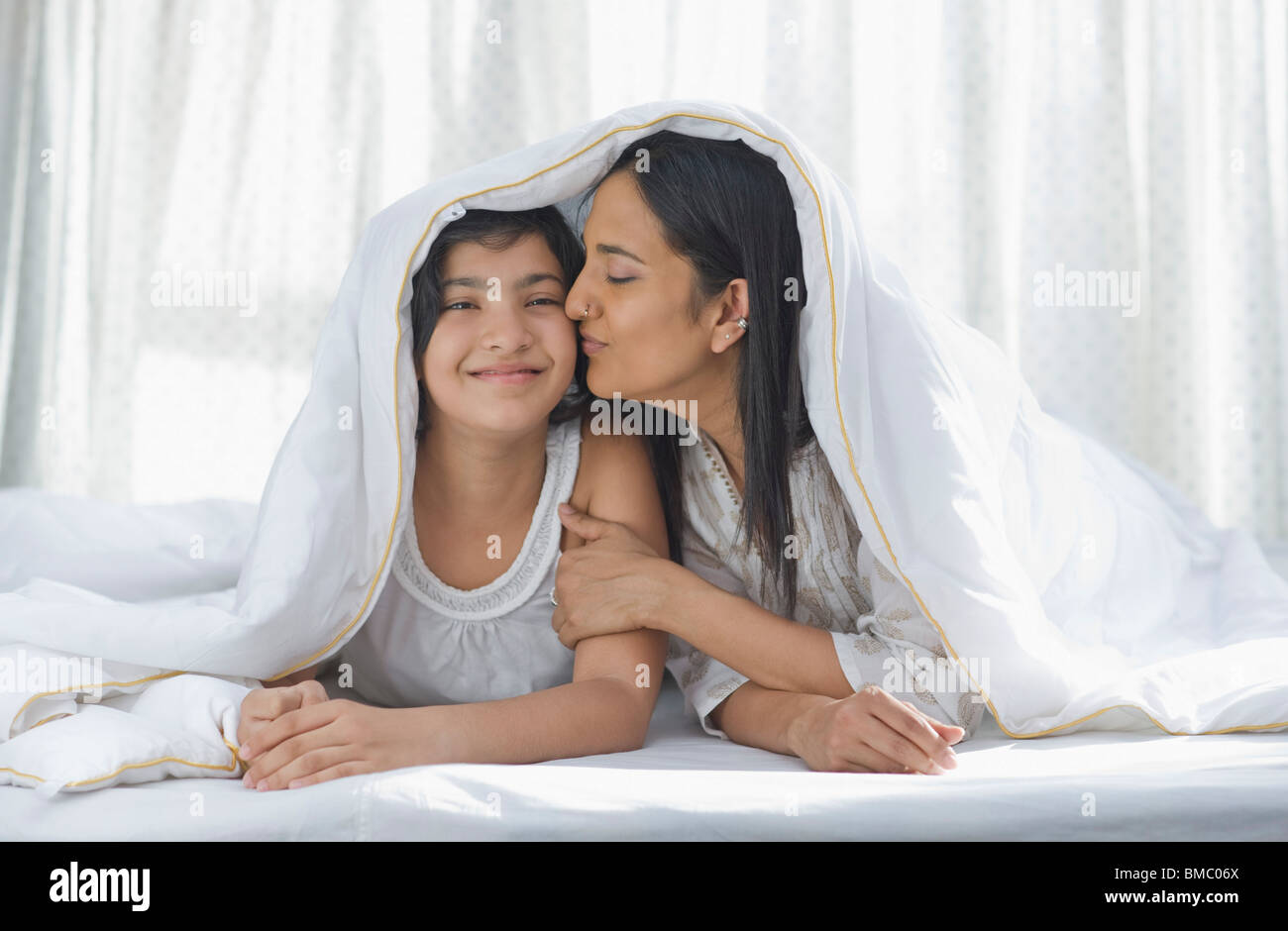 Woman lying on the bed and kissing her daughter Stock Photo