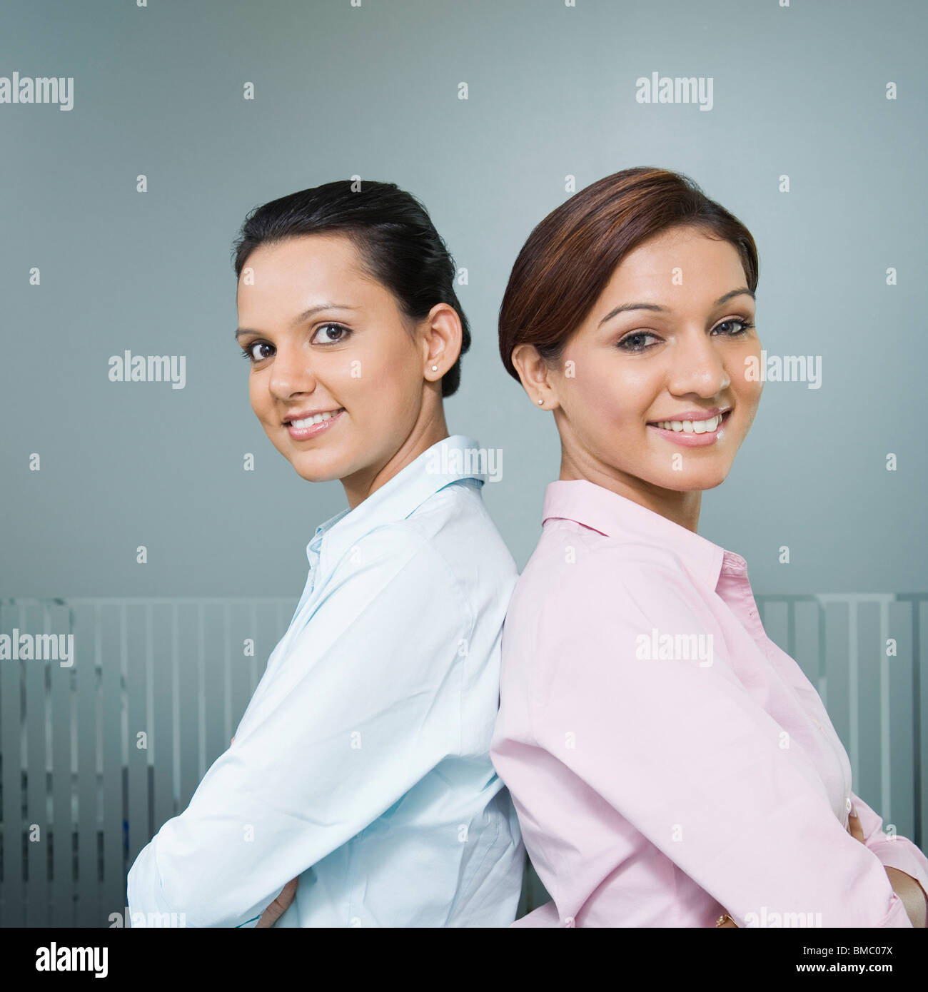 Two businesswomen standing back to back and smiling Stock Photo - Alamy