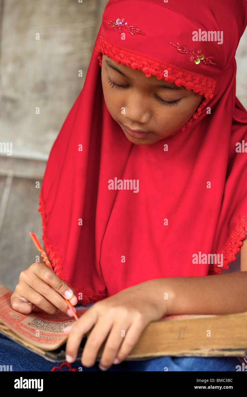 Young muslim girl wearing red veil concentrating on reading Quran, East Java, Indonesia Stock Photo