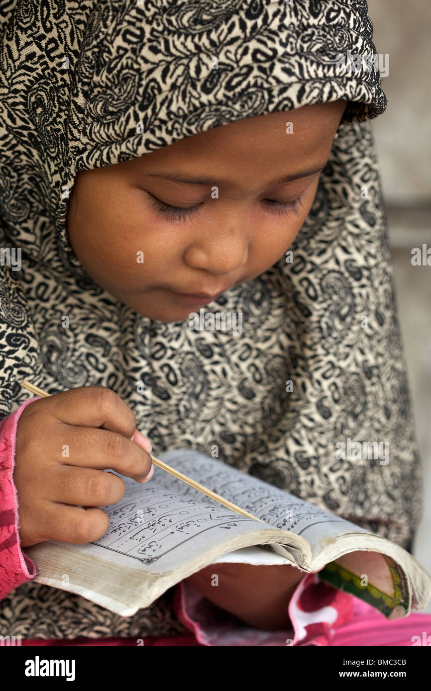 Young muslim girl wearing a veil concentrating on reading Quran, East Java, Indonesia Stock Photo