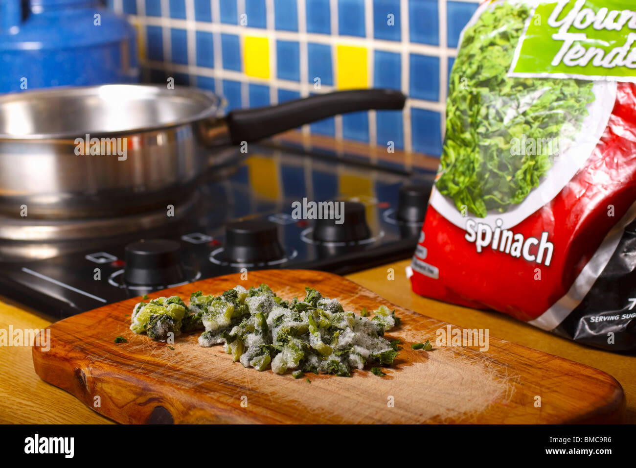 Frozen spinach on a cutting board beside counter-top stove. Foreground focus. Stock Photo