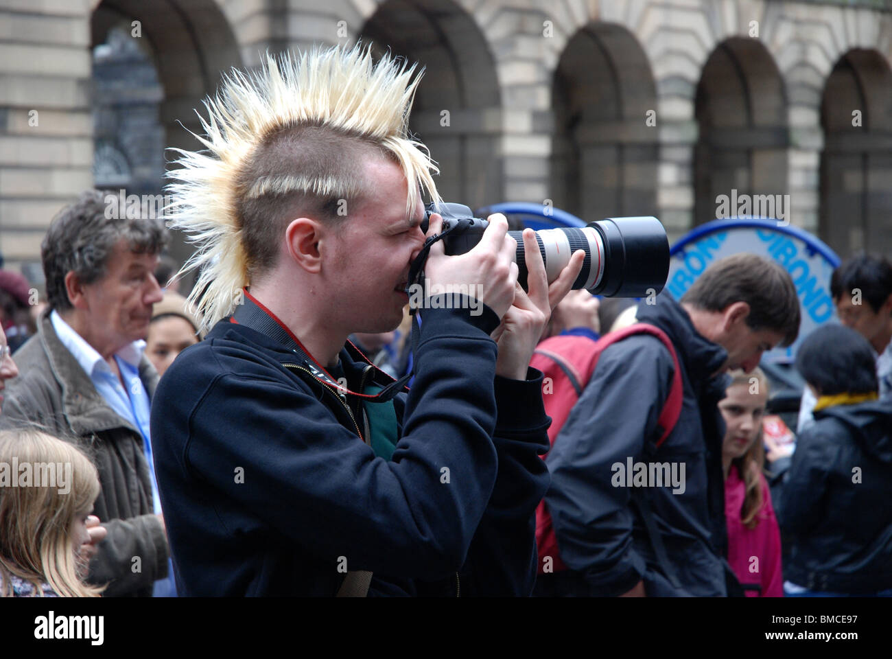 A photographer with a punk mohican hairstyle on the High Street in Edinburgh during the Fringe Festival. Stock Photo