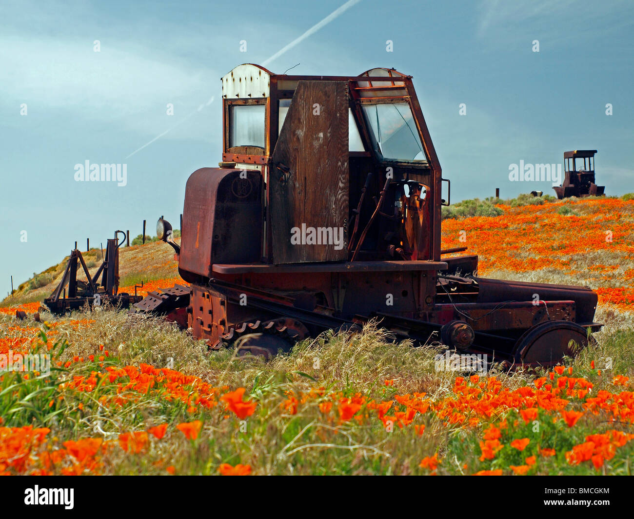 An old tractor and other farm equipment lie rusting in a field of wildflowers. Possible International TD 14 tractor. Stock Photo