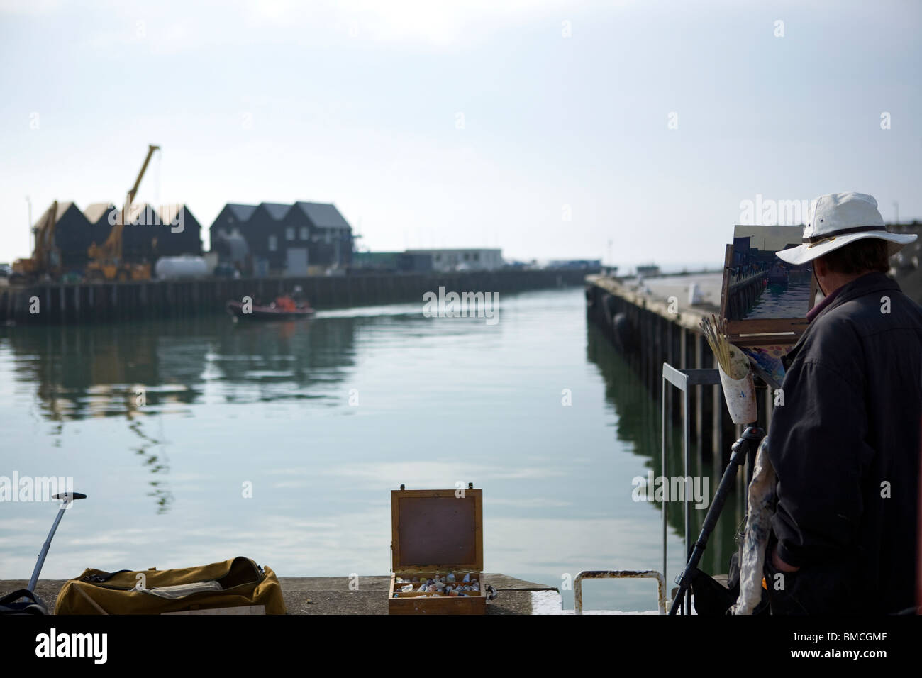 Artist painting landscape of Whitstable harbour showing the reflection in the sea using a paint brush and oil on canvas Stock Photo
