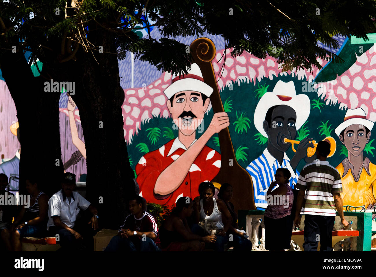 People sit in a park by a large mural depicting musicians in Baracoa, Cuba on Monday July 14, 2008. Stock Photo