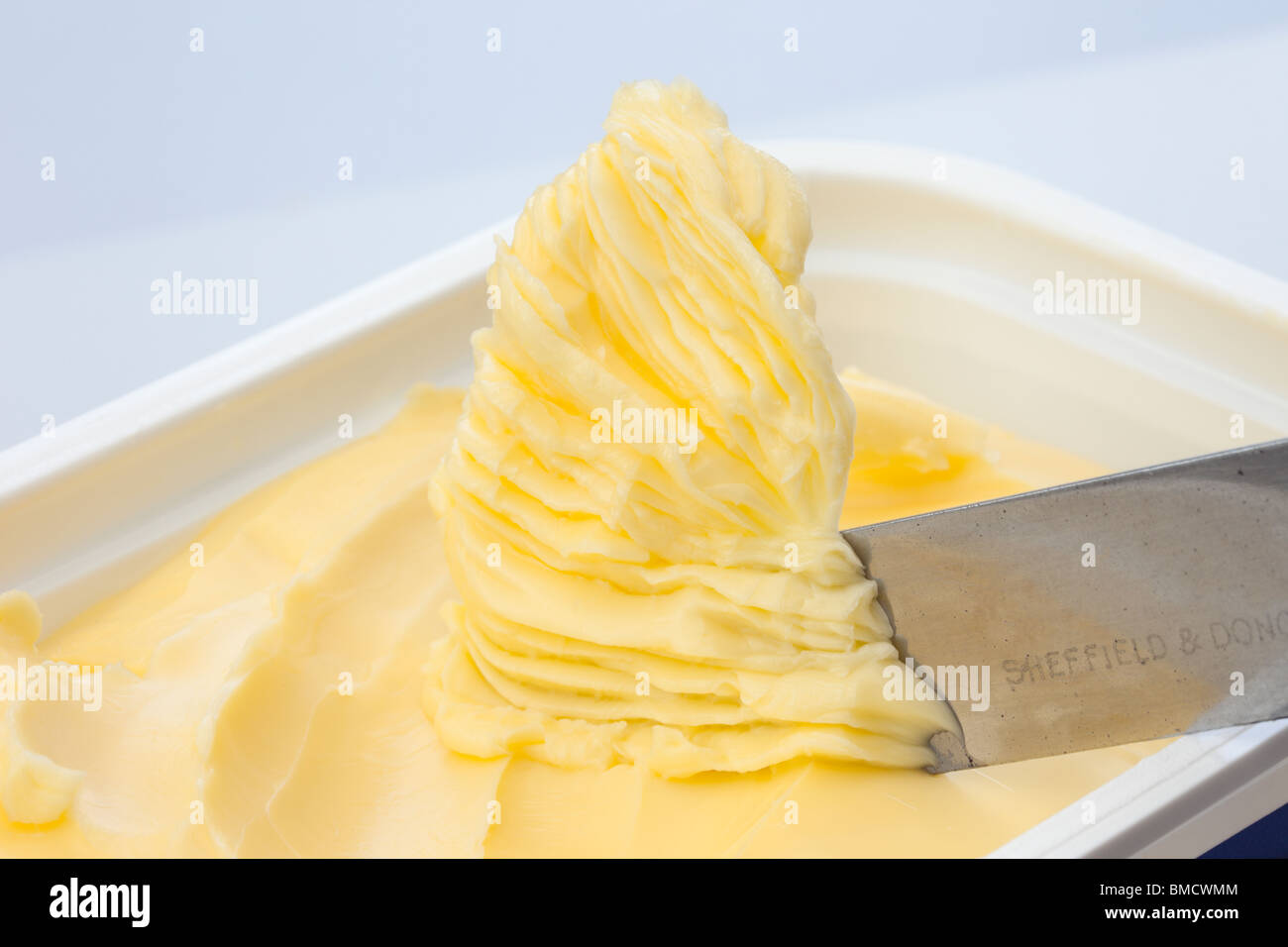 Knife scooping up spreadable dairy spread in a plastic tub container Stock Photo