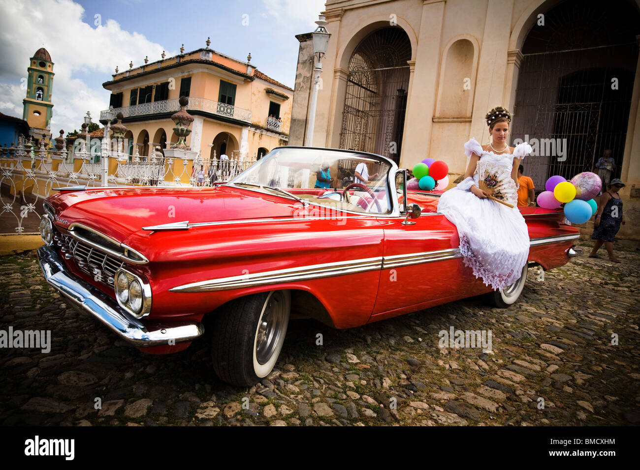 Fourteen-year-old girl sits on a vintage car as she poses for a photo on the day of her Quinceanera party in Trinidad, Cuba Stock Photo