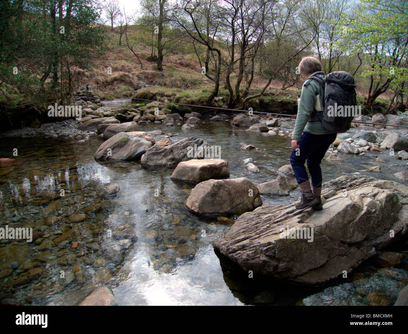Walker on stepping stones, crossing river, Lakes, UK Stock Photo