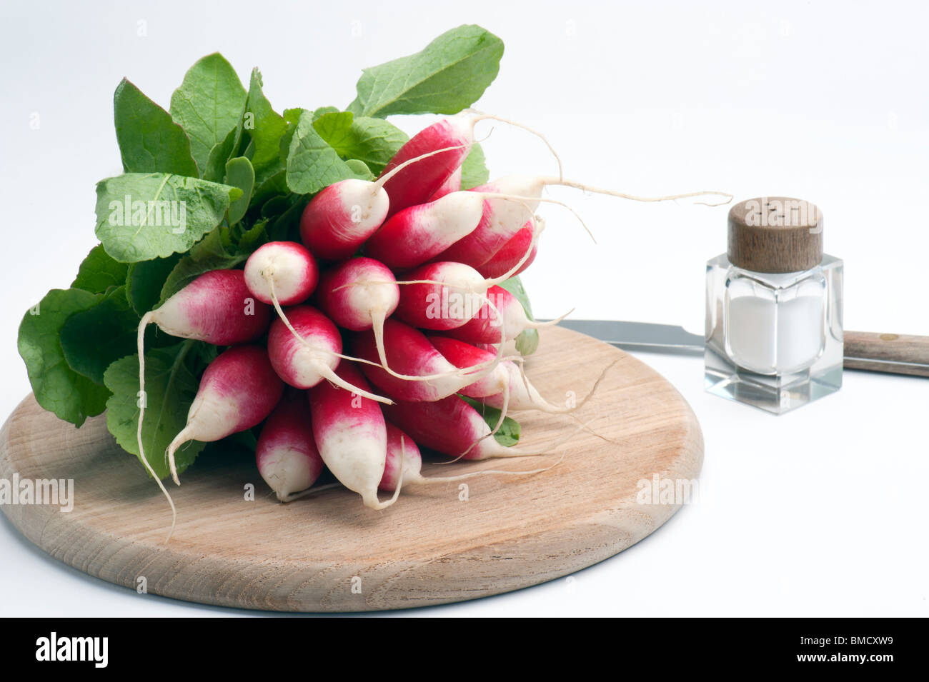 French Breakfast Radish On A Wooden Chopping Board, With A Salt Pot and Knife, Against A White Background Stock Photo