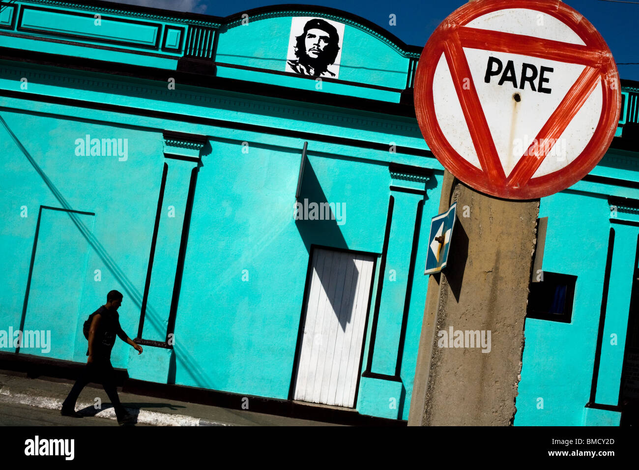 A man walks by a bright blue building adorned with an image of Ernesto Che Guevara in Baracoa, Cuba on Monday July 14, 2008. Stock Photo