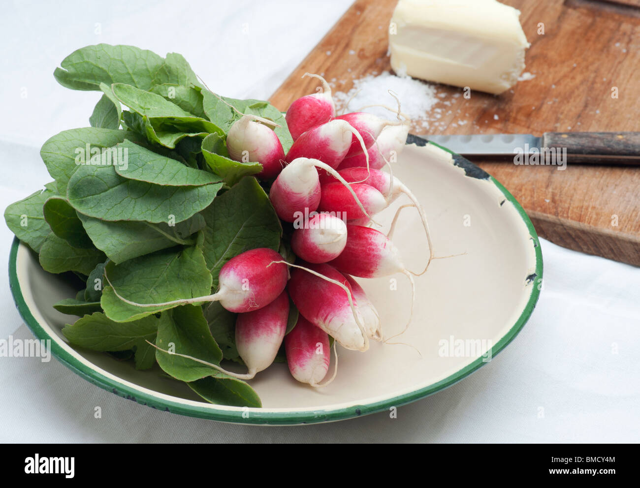 Fresh Radishes In An Enamel Dish, With Butter, Salt and A Knife In The Background Stock Photo