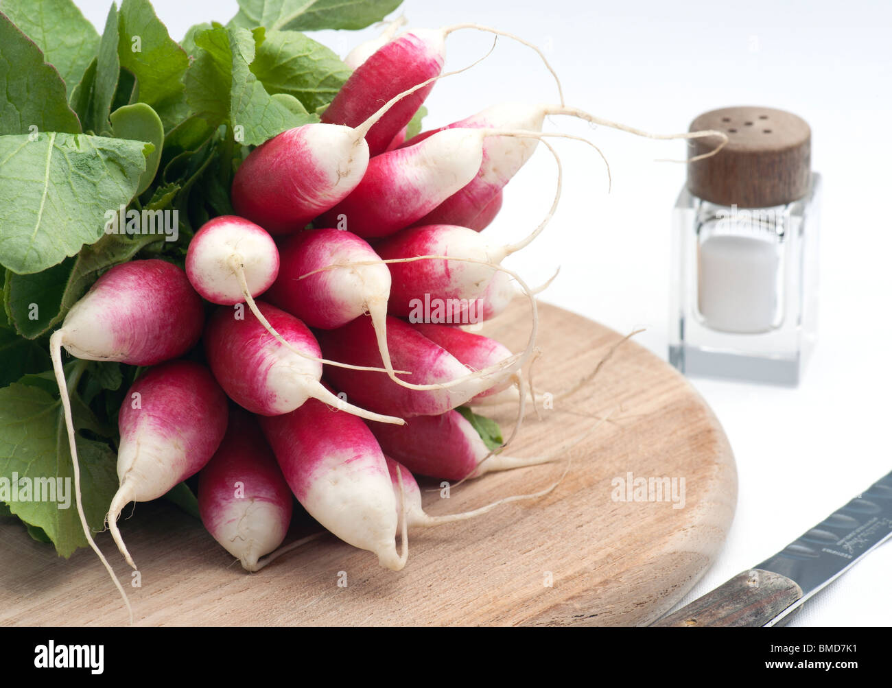 A Bunch Of Fresh French Breakfast Radish On A Wooden Chopping Board, With A Salt Pot and knife, On A White Background Stock Photo