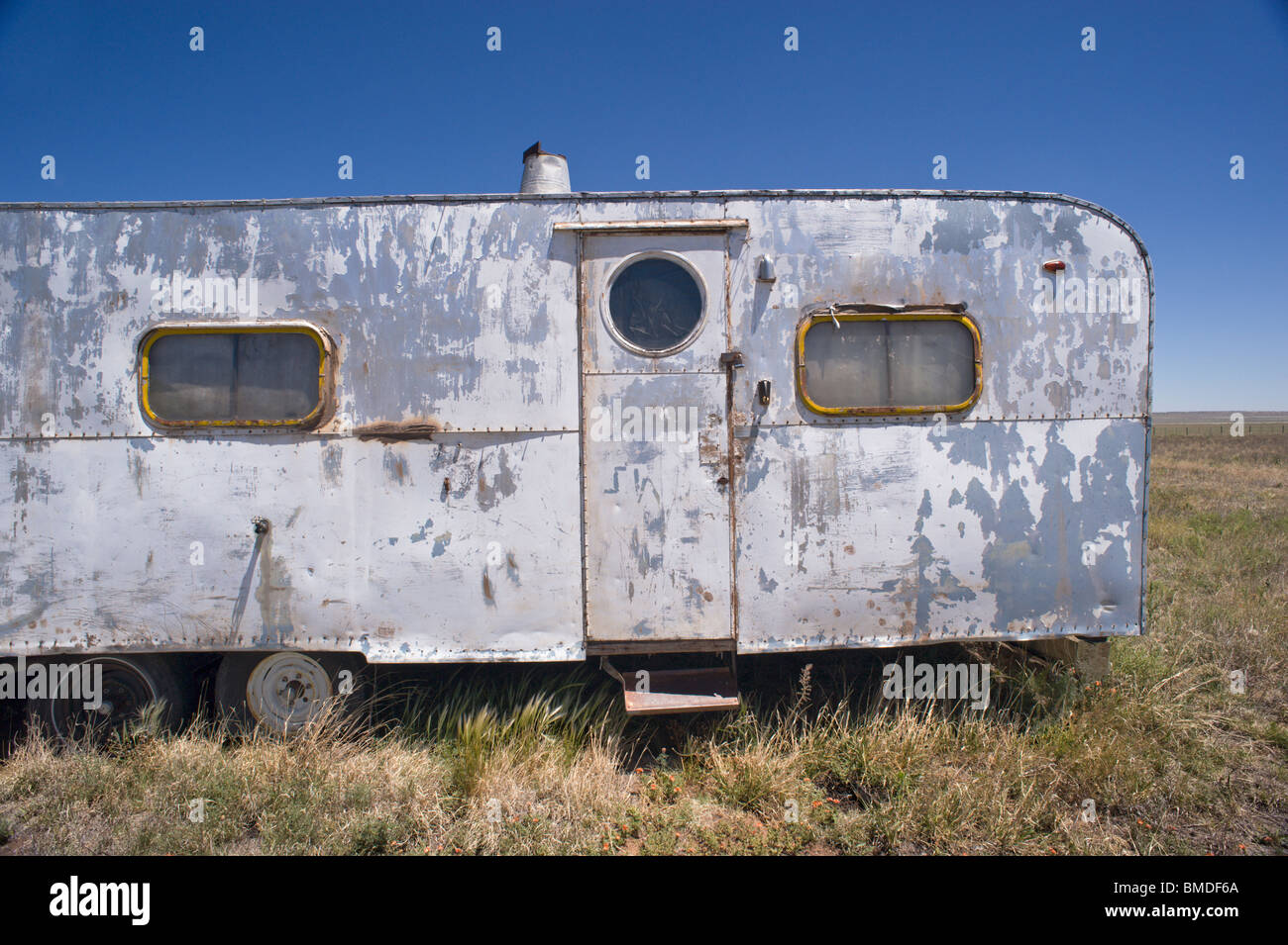 A frequent sight in New Mexico - a dented, paint-peeling, derelict camping trailer sitting in a weed-patch - Encino, New Mexico. Stock Photo
