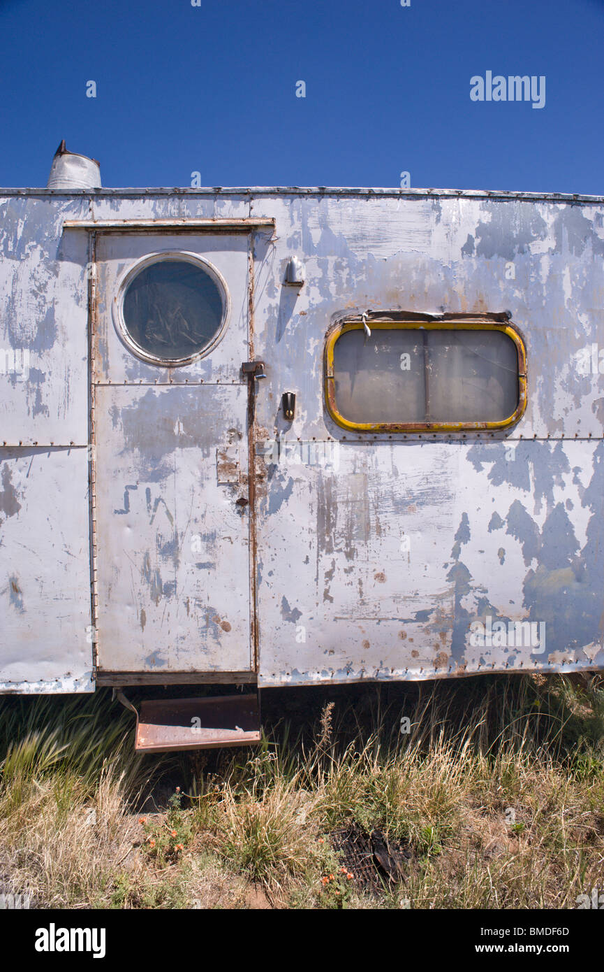 A frequent sight in New Mexico - a dented, paint-peeling, derelict camping trailer sitting in a weed-patch - Encino, New Mexico. Stock Photo