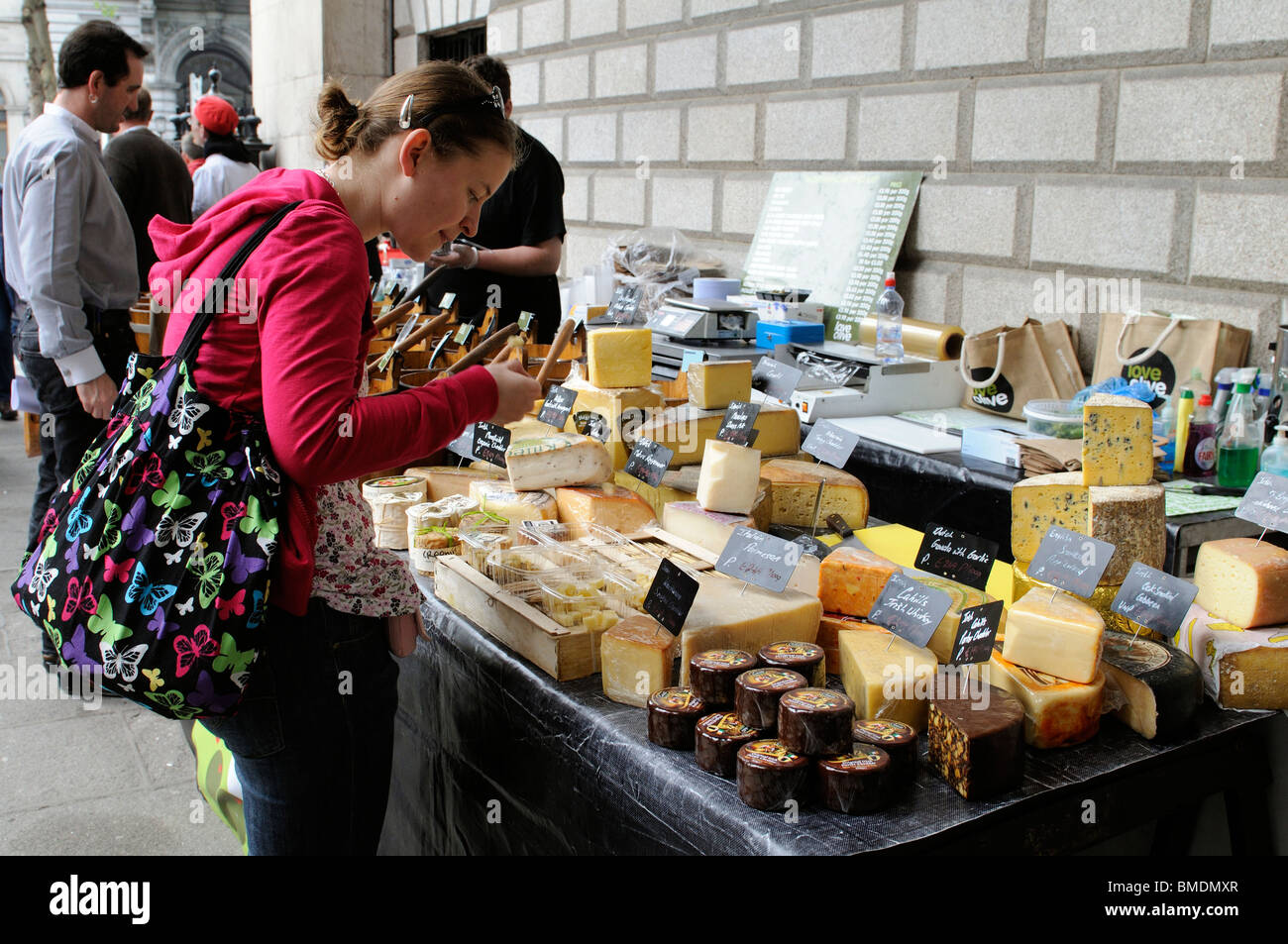Young woman selecting cheeses from a farmers market cheese stall out