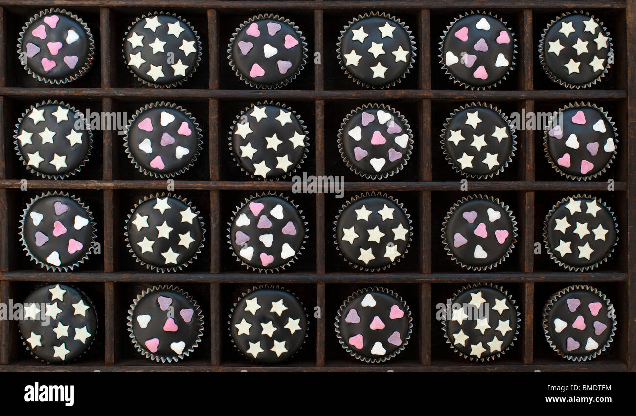 Mini cupcakes decorated with black icing, sugar hearts and white chocolate stars in a wooden tray Stock Photo