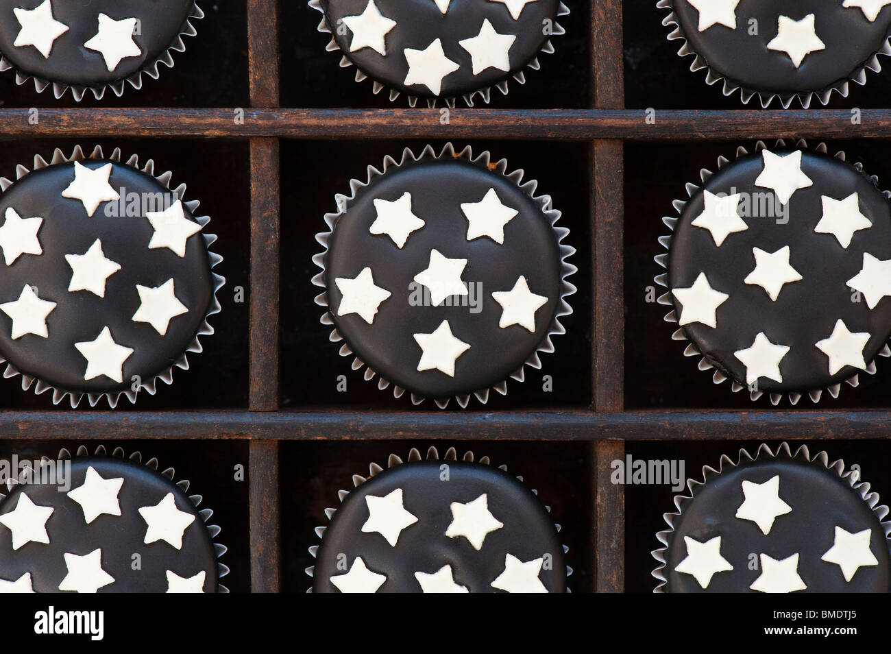 Mini cupcakes decorated with black icing and white chocolate stars in a wooden tray Stock Photo