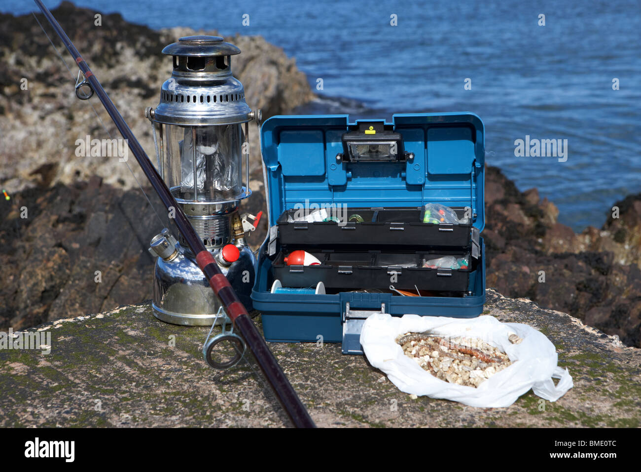 fishing tackle box filled with sea fishing gear rod pressure lamp and bag of ragworm bait on the county antrim coast Stock Photo