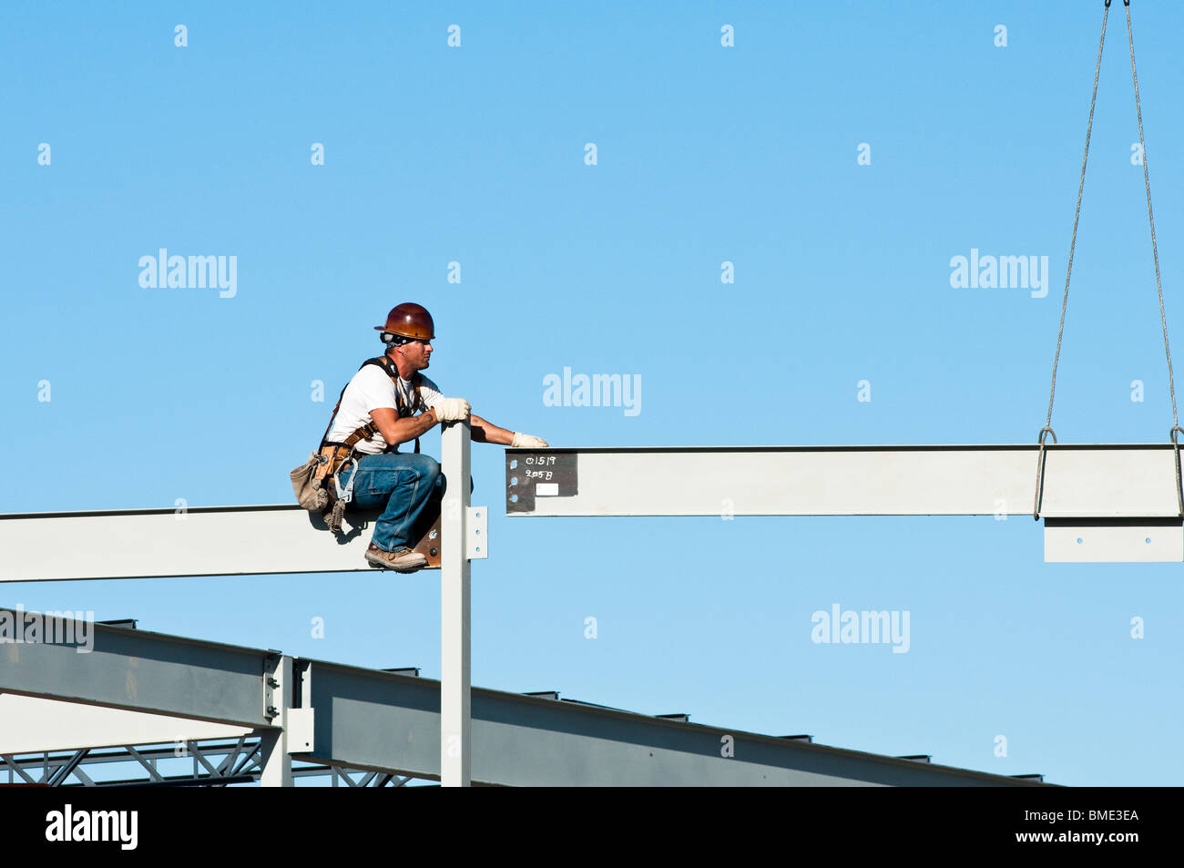 a steelworker guides a beam into position as part of the structural ...