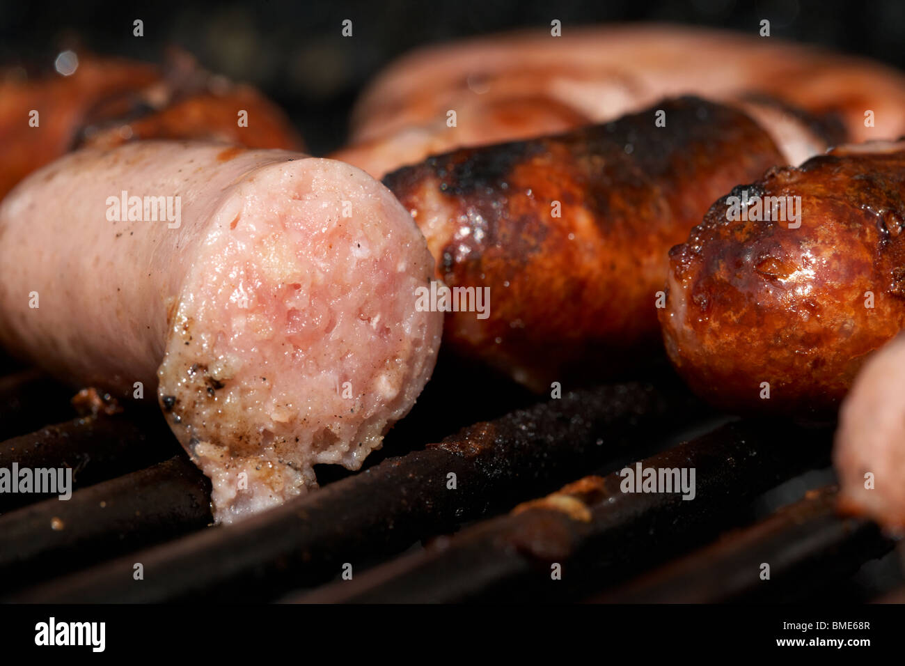 raw uncooked organic fresh irish pork sausages next to fully cooked sausage cooking on a barbeque Stock Photo