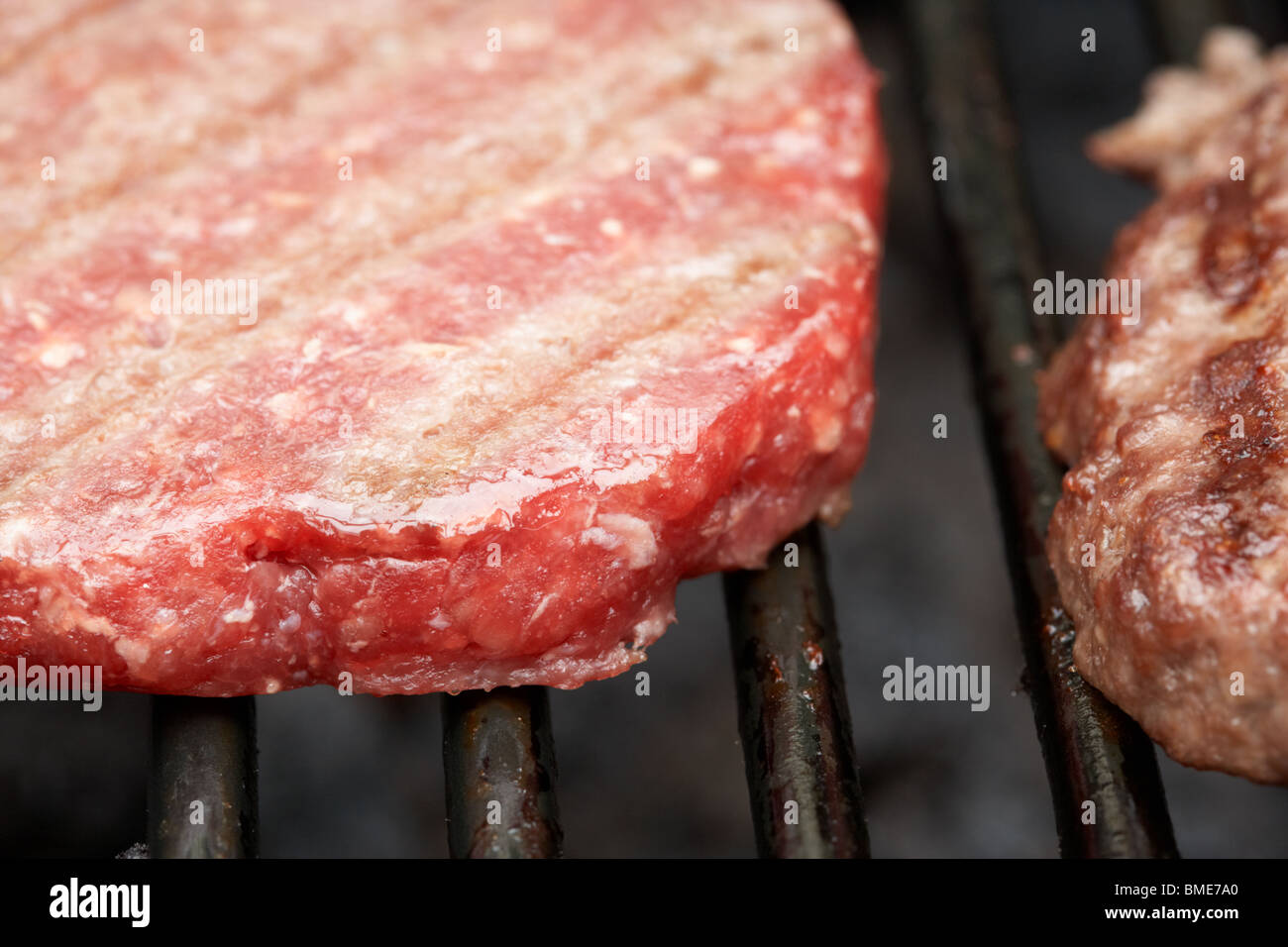 partially raw steak burgers cooking next to a cooked burger on a barbeque grill Stock Photo