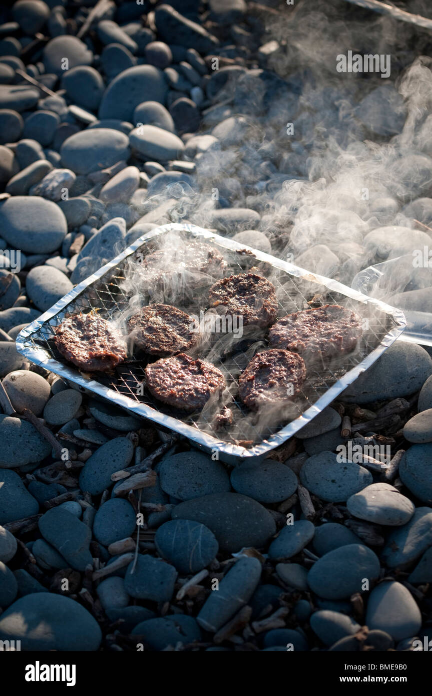 cooking beef burgers on a cheap disposable barbecue on a beach, UK Stock Photo
