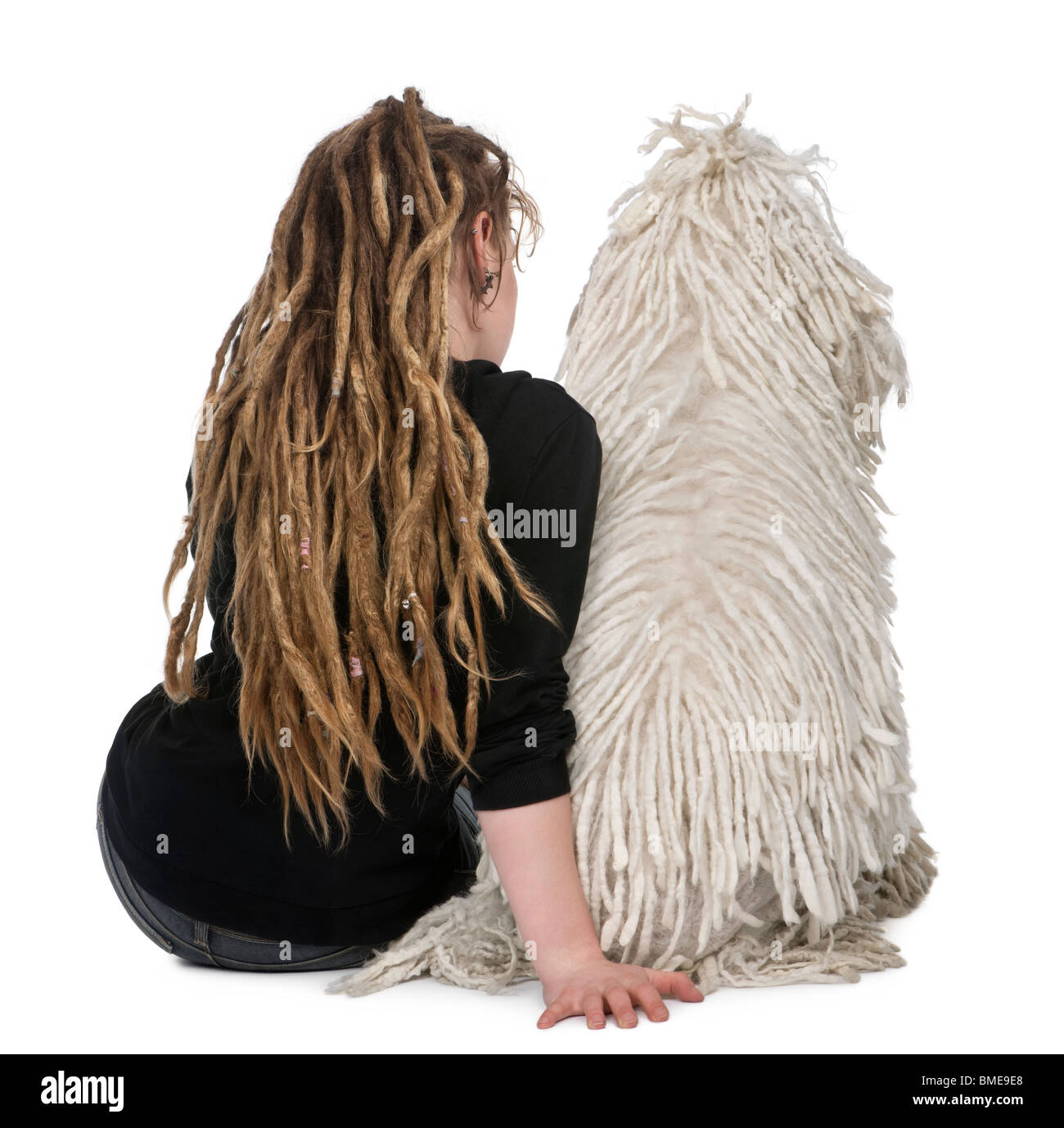 Rear view of a White Corded standard Poodle and a girl with dreadlocks sitting in front of white background Stock Photo
