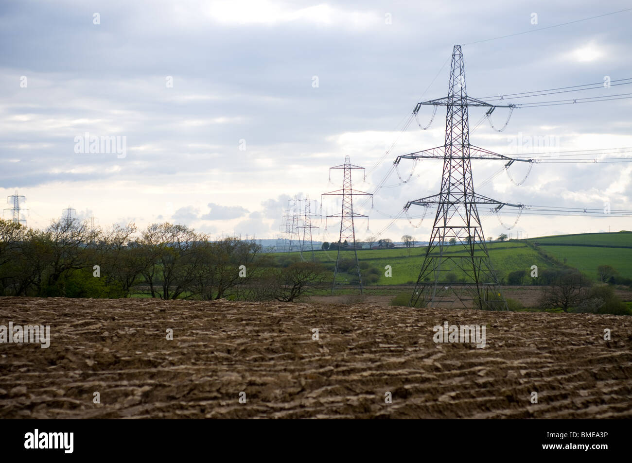 Electricity pylons in front of a ploughed field Stock Photo