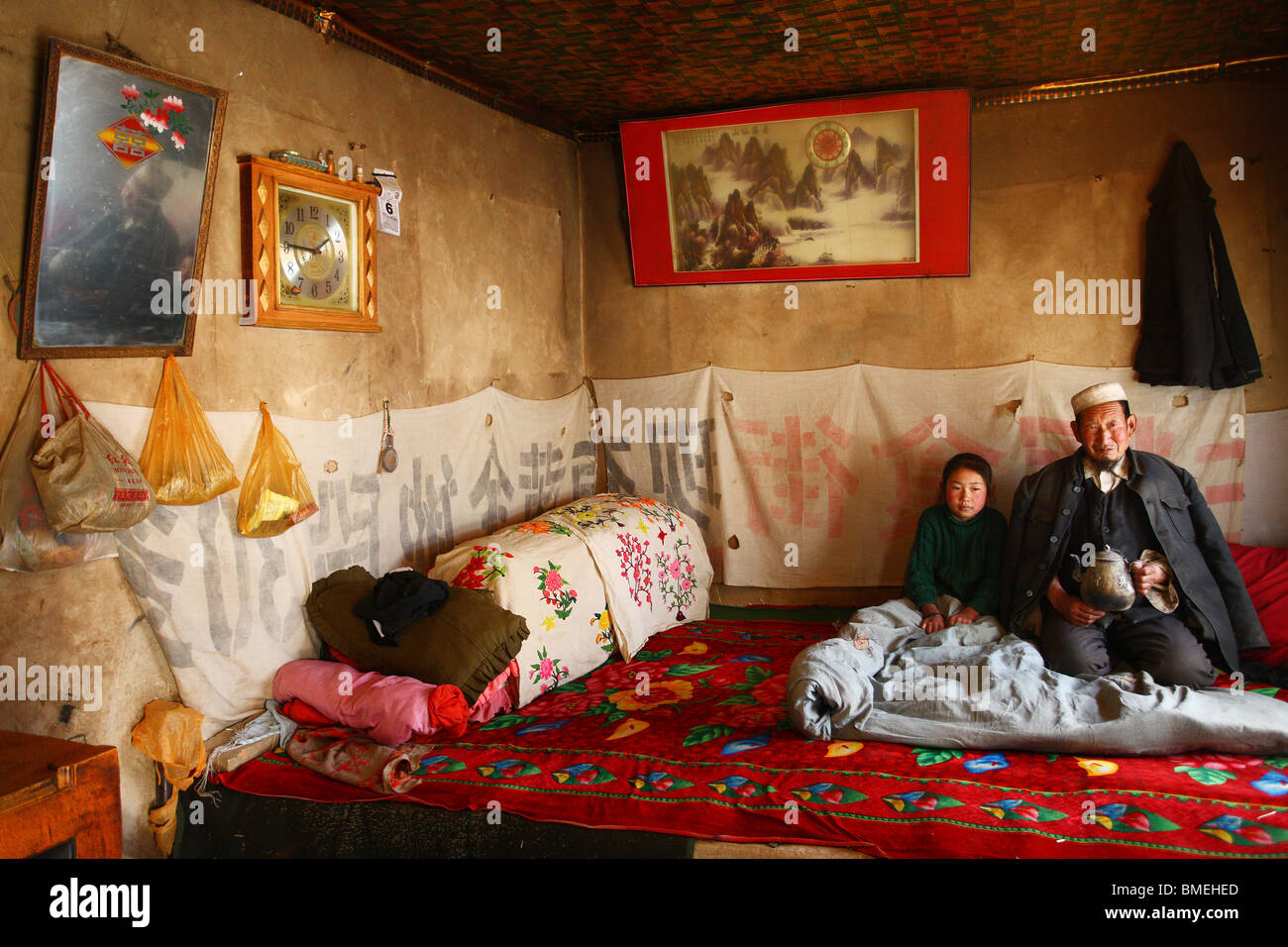 Elderly Salar man on Kang bed-stove with his granddaughter, Xunhua Salar Autonomous County, Haidong, Qinghai, China Stock Photo