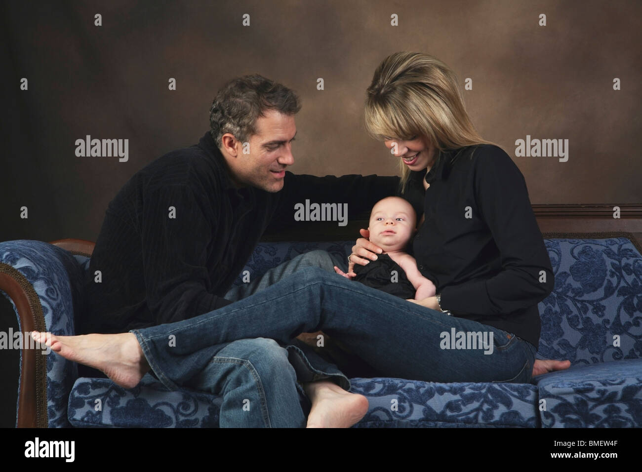 A Family Sitting On A Couch Holding Their Baby Stock Photo