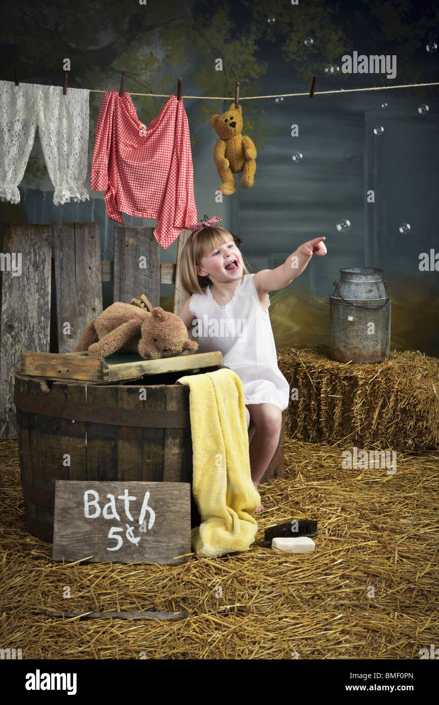 A Girl Pointing At Bubbles And Standing Beside A Barrel With A Bath Sign Stock Photo