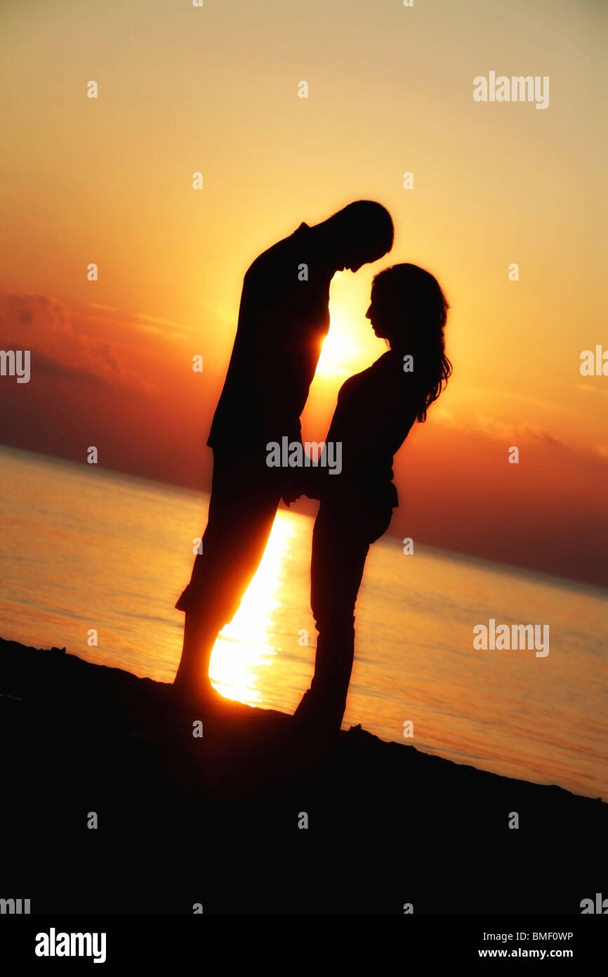 A Man And Woman Facing Each Other And Holding Hands While Standing On The Beach In The Sunset Stock Photo